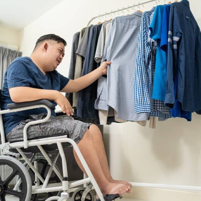 Asian Young Man With Autism Choosing Clothes On Closet Rack